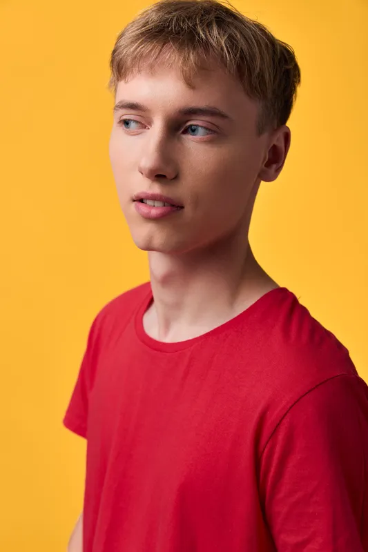 Young man in a red shirt against a vibrant yellow background, relaxed pose and neutral expression, casual fashion aesthetic, studio lighting and clean composition for lifestyle and advertising