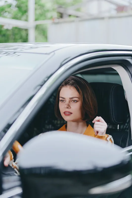 car, driver, woman, a focused woman sits in the driver's seat of a sleek car, eyes ahead and hands on the wheel, conveying confidence, readiness, and calm for a journey.
