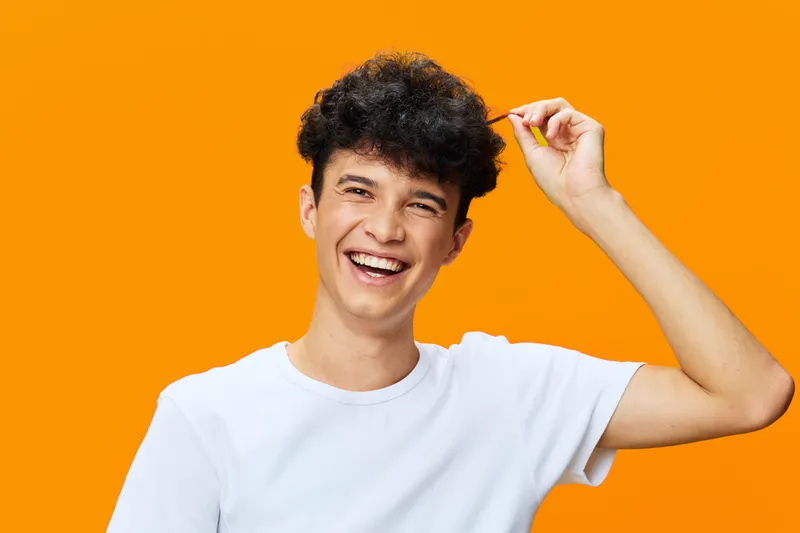 smiling young man with curly hair wearing white t-shirt on vibrant orange background, happy expression, casual style, bright color contrast