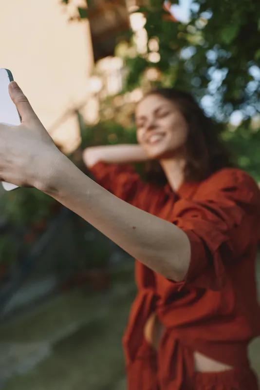 A young woman in a red robe takes a casual selfie outdoors, turning a private moment into a candid lifestyle shot that conveys spontaneity, confidence and relaxation