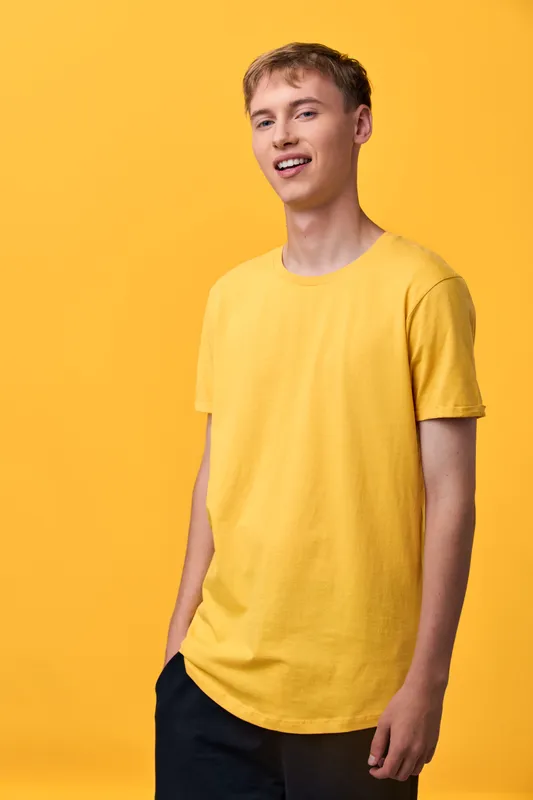 Yellow shirted man in casual fashion stands in a studio with a bright background, conveying relaxed youthfulness and approachable style for lifestyle or fashion campaigns