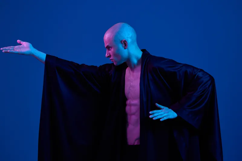 Dynamic man striking a pose in a flowing black robe, showcasing strength and elegance against a vivid blue background. Perfect for artistic concepts and themes.