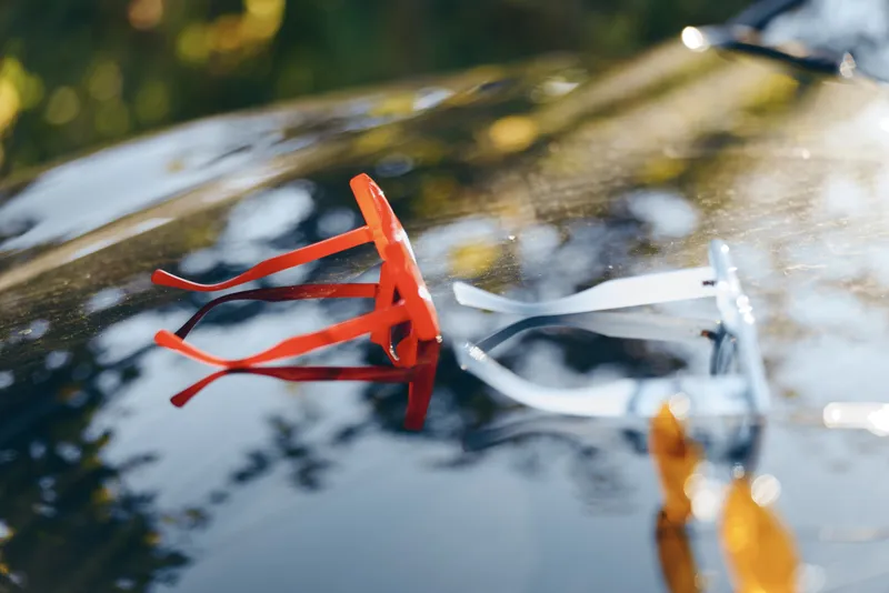 A reflective close up of sunglasses resting on a glossy car hood, sunlight dances across the surface, creating a stylish, casual mood and a sense of travel and summer freedom.