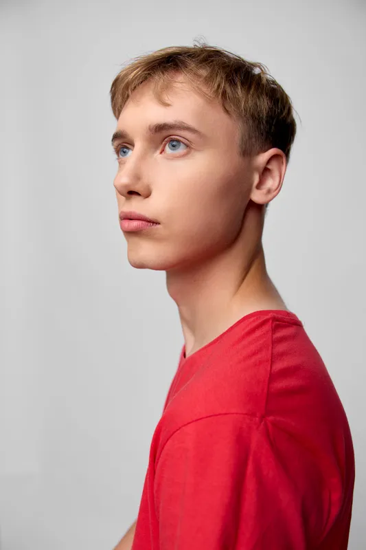 Youth, teen, man, looking, thoughtful, profile, red, shirt, studio image showing a calm gaze and clean background, highlighting contemporary fashion, minimalism, and studio lighting in a studio