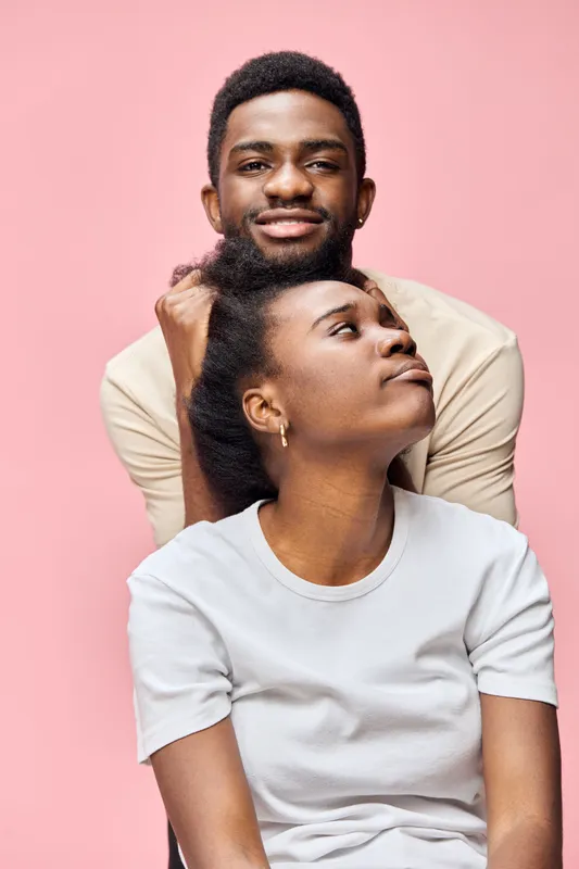 A young African couple poses together against a pink background, showcasing emotions of love and connection, ideal for themes of relationships and intimacy