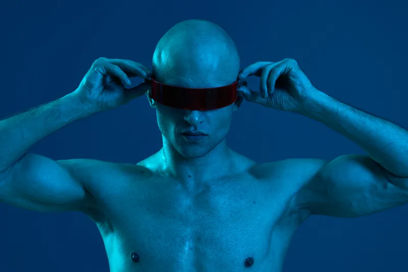 A futuristic man adjusting red-tinted glasses, with a striking blue light illuminating his body. This captivating black and white image showcases innovation and technology.