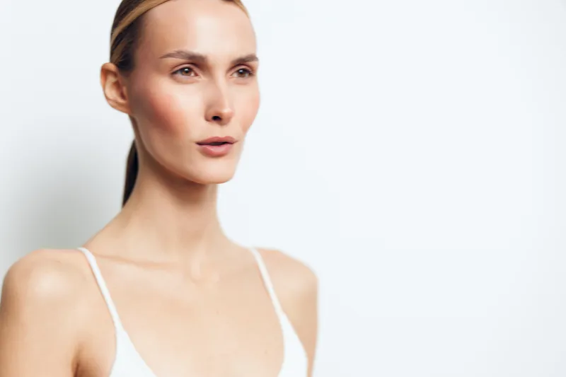 Portrait of focused woman with light skin and blonde hair in white top, looking away, minimal makeup, clean background, natural light, serene expression, soft shadows