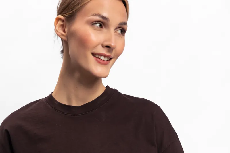 Smiling young woman with neat hair wearing dark sweater looks aside with soft expression. Studio portrait on white background with natural makeup and casual style concept.
