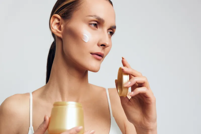 Woman skincare cream serum face beauty moisturizing jar closeup, applying moisturizer on clean studio background, calm expression, self care for daily hydration