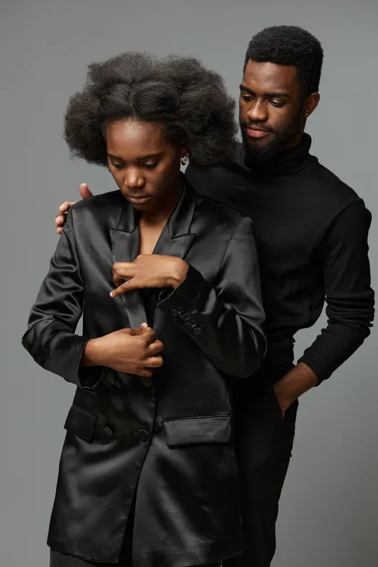 A stylish African couple in elegant attire conveys deep emotions in a minimalist gray background, showcasing confidence, intimacy, and sophistication