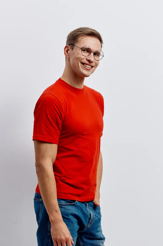 smiling man standing in casual red t-shirt and blue jeans wear eyeglasses look camera happy cheerful isolated on light background digital nomad concept