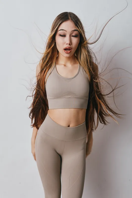 Young woman in beige sportswear with long hair standing with closed eyes in studio, fitness apparel and healthy lifestyle concept for training and workout.