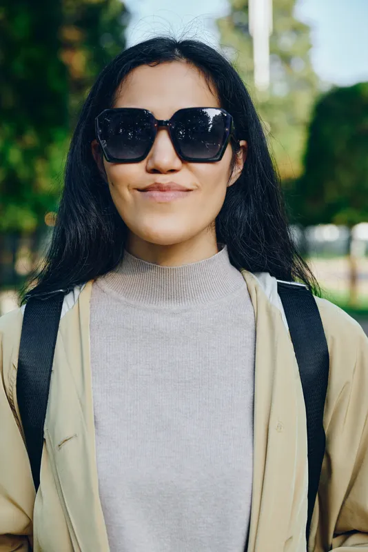 Sunglasses, outdoor park setting, casual style, backpack straps, smiling woman enjoying daylight and nature in a relaxed lifestyle moment for photography