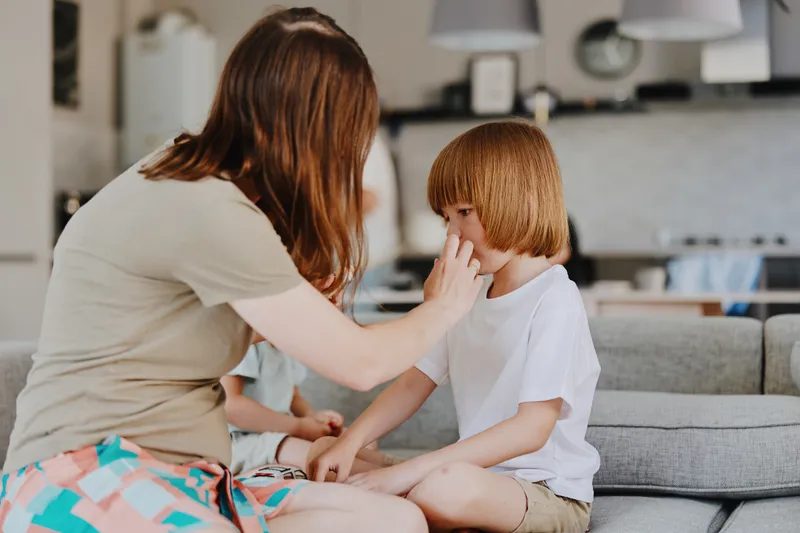 Caring woman gently attending to her child in a cozy home environment, showcasing nurturing love and family connection.