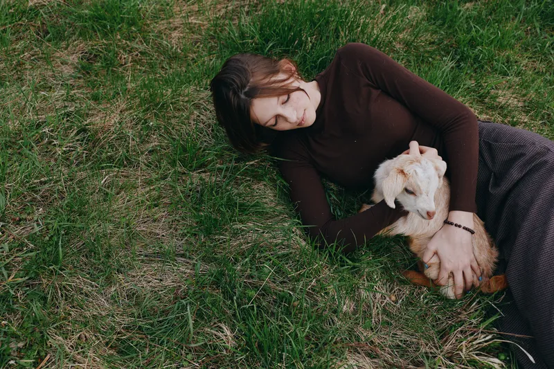 Lifestyle scene with a woman lying on grass, gently stroking a dog, creating a calm outdoor moment of affection, companionship and serenity, under natural light for a relaxed, everyday mood.