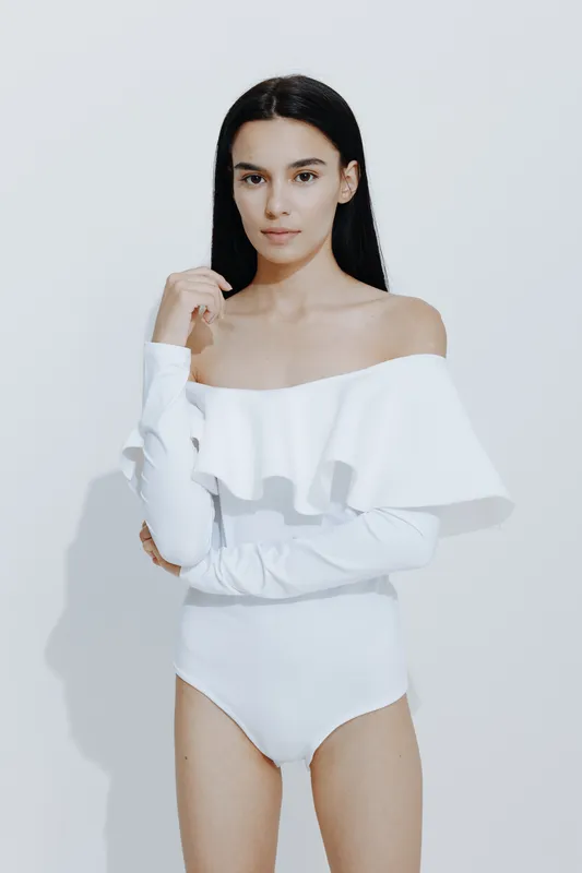 Sport fitness woman in white outfit stands confidently against a plain background, showcasing strength, focus, and an athletic physique in a minimalistic setting.