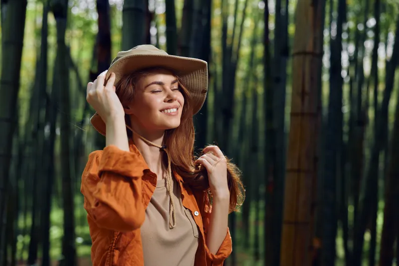 Woman smile hat bamboo forest nature portrait happy female traveler in straw hat enjoying sunlight among tall bamboo stalks, relaxed outdoor lifestyle and peaceful green escape.