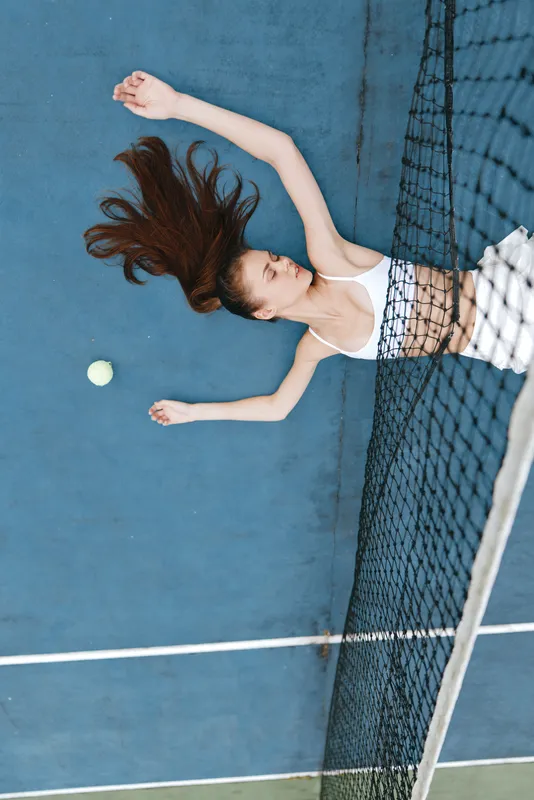 Young athletic woman in sportswear playing tennis, showcasing focus and determination with a green tennis ball and blue court as the backdrop