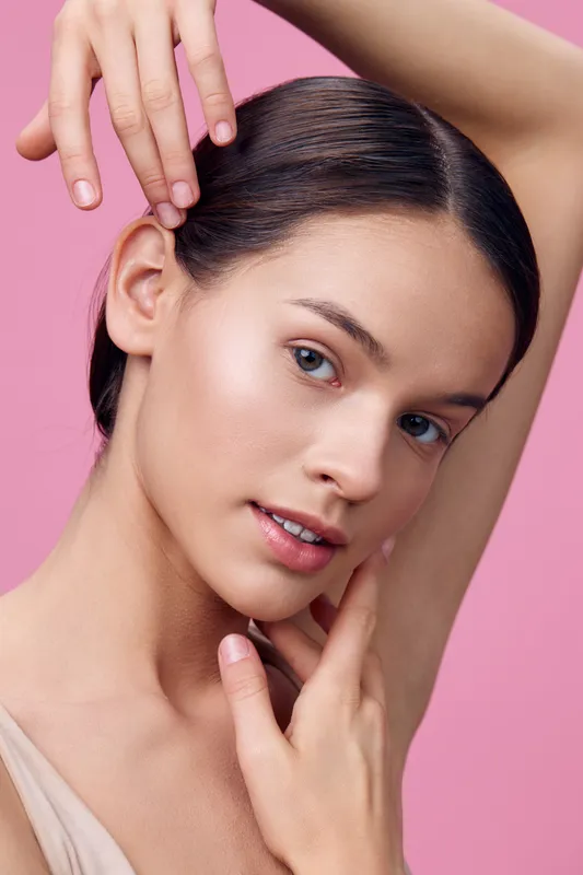 Young woman with smooth skin and subtle makeup poses elegantly against a soft pink background, embodying beauty, confidence, and serenity for skincare and beauty concepts