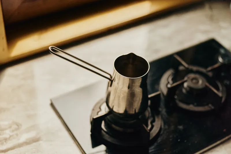 Close up of a stove burner and metal pot on a kitchen counter, warm lighting highlights the metallic surface, creating a simple and practical cooking scene.