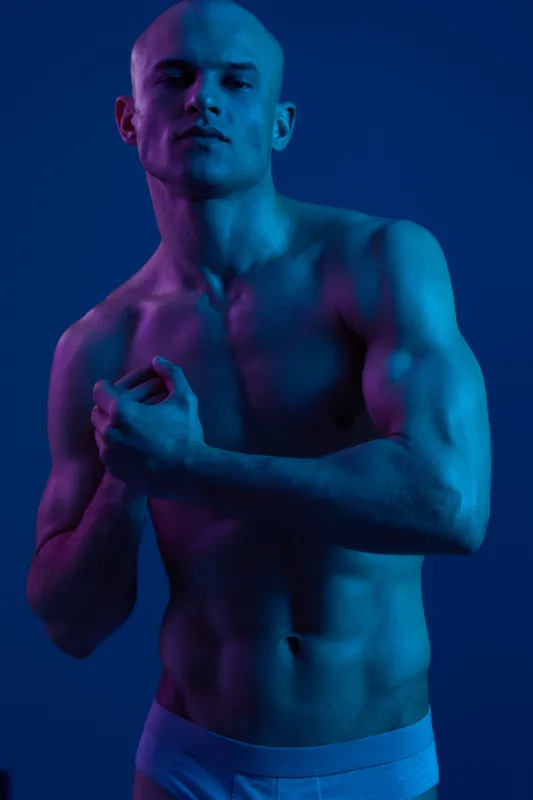 Athletic man posing under vibrant blue and purple lights, showcasing strong features and a confident demeanor. A striking display of modern portrait photography.