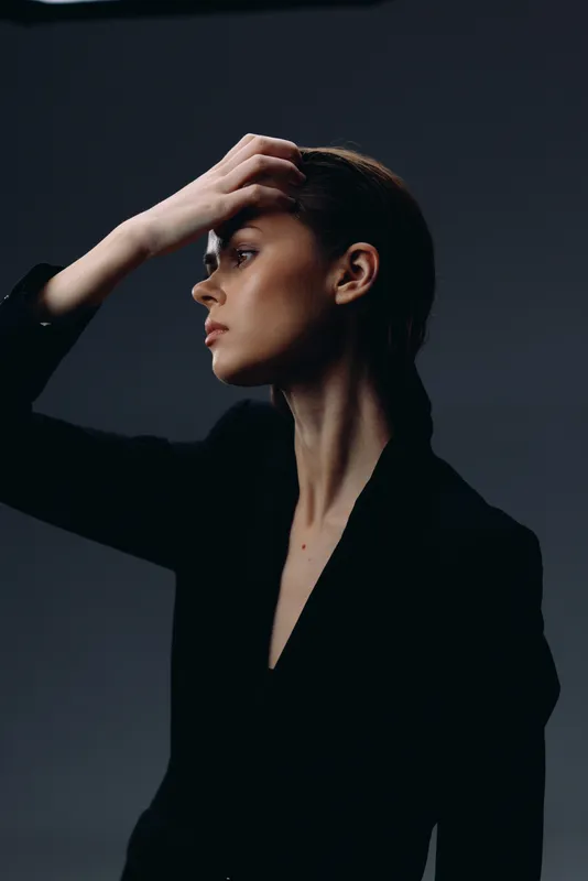Profile of a thoughtful woman in black outfit with hand on head against dark background