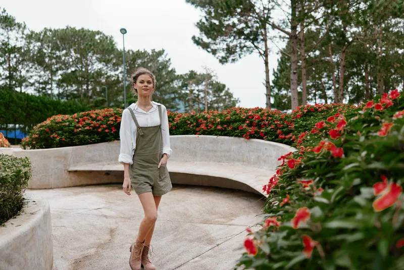 Young woman in casual summer outfit walking through a floral park, showcasing joy and confidence, surrounded by vibrant flowers and greenery