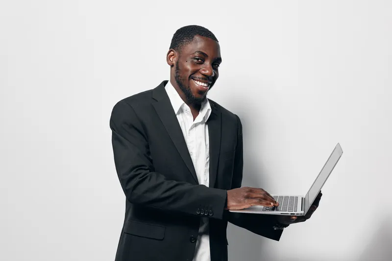 African American man in black suit using laptop and smiling for business, technology and communication with confident professional on white background.