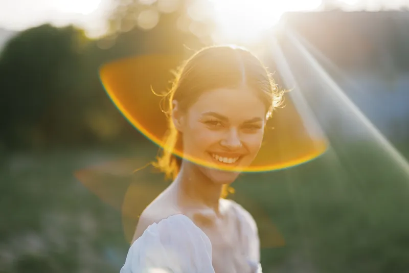 A joyful young woman smiling in a sunlit outdoor setting, showcasing vibrant colors and a warm, cheerful emotion, ideal for seasonal and lifestyle themes