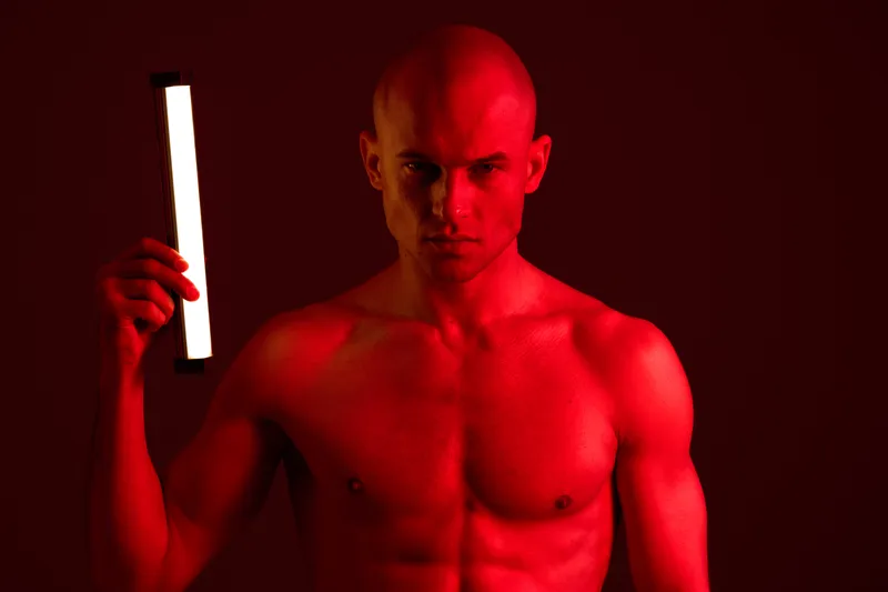 Intense man holding a light stick in a dramatic red background, showcasing strong emotions and a striking look, emphasizing the play of light and shadow.