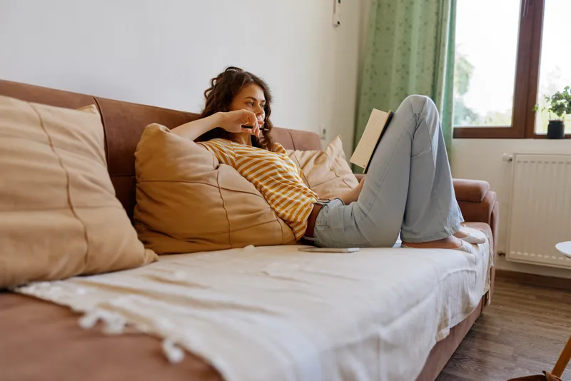 Woman relaxing at home on a sofa with a tablet, casual and comfortable, enjoying downtime in a cozy living room setting, soft light, warm tones, cushions, modern decor, everyday life.