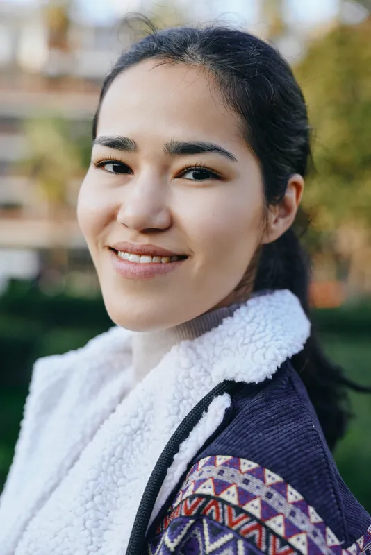 Smiling woman outdoors in a patterned jacket and fluffy fleece, showcasing casual fashion, confidence, and sunny daytime ambiance in a relaxed outdoor setting