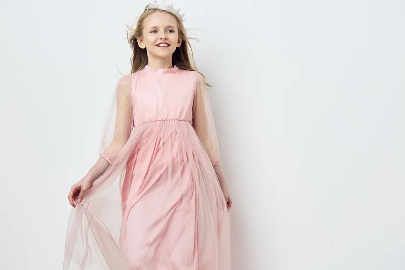 Happy girl in a flowing pink dress posing against a minimalist white background, showcasing joy, innocence, and elegance in a soft, serene atmosphere
