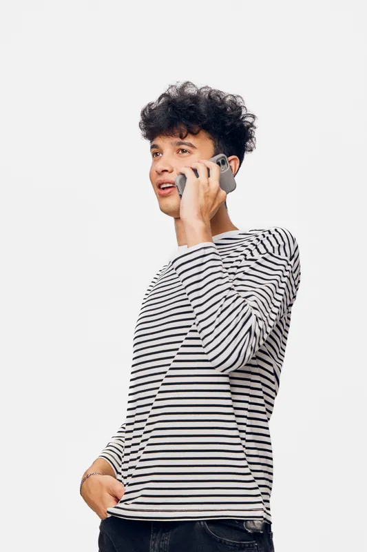 Young man with curly hair talking on smartphone wearing striped long sleeve shirt, casual style, isolated white background, communication concept photo.