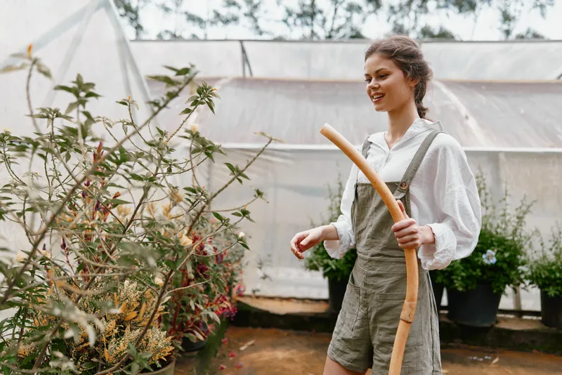 Young woman in overalls tending to plants in a greenhouse, showcasing a connection to nature and healthy living, with a bright and fresh atmosphere