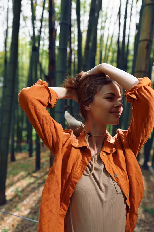 Woman forest bamboo orange portrait smiling outdoors nature relaxation peaceful casual moment as she poses in an orange jacket with sunlight through trees, serene leisure and happy mood