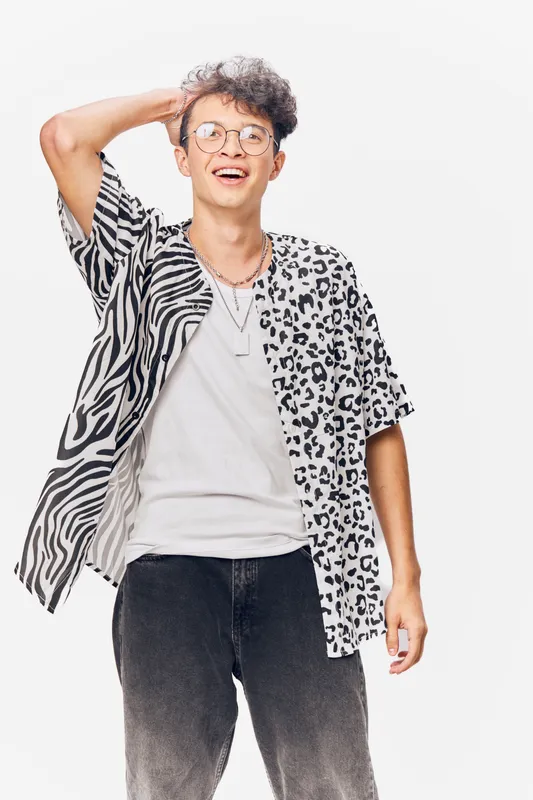 young man wearing a casual animal print shirt smiling confidently with glasses and curly hair on white background, stylish and relaxed vibe
