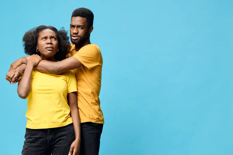 Couple in matching yellow shirts expressing confusion and concern against a bright blue background, showcasing emotional connection and casual style
