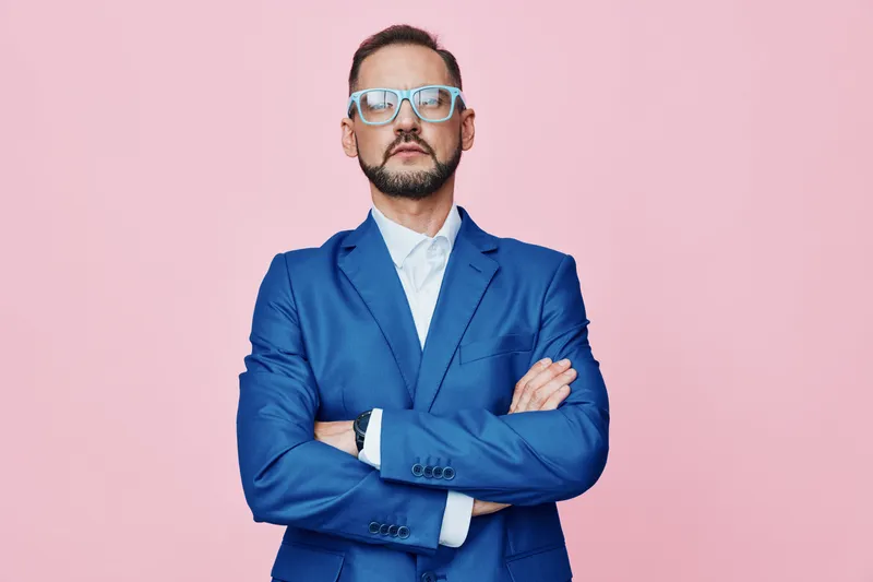Professional businessman stands confidently against a solid pink backdrop, showcasing focus, determination, calm authority, and poised posture that communicates leadership.