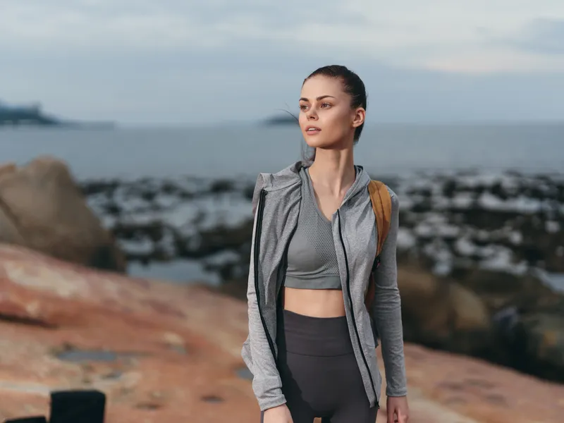 Young woman in sporty clothing standing by the seaside, portraying confidence and a healthy lifestyle amidst a serene natural backdrop