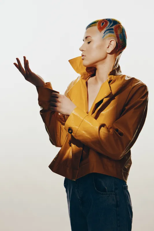 woman with colorful hair art in a yellow jacket posing thoughtfully, stylish casual outfit, creative hairstyle, isolated on white background