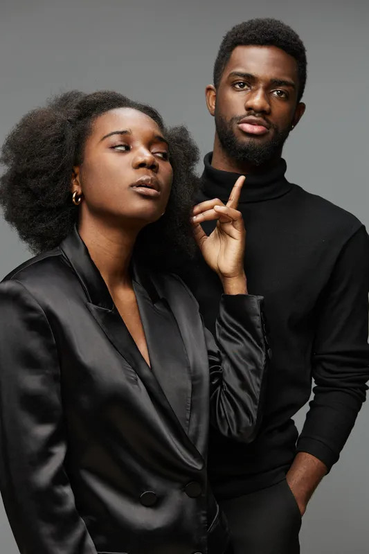 Stylish couple portrait showcasing a confident African couple in chic black outfits against a minimal gray backdrop, embodying modern elegance and emotional depth