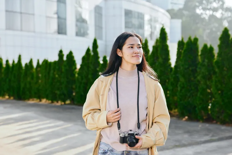Woman with camera in a casual beige jacket outdoors, urban backdrop and soft sunlight, a thoughtful street style scene ready for a shoot, candid mood with modern architecture in the background