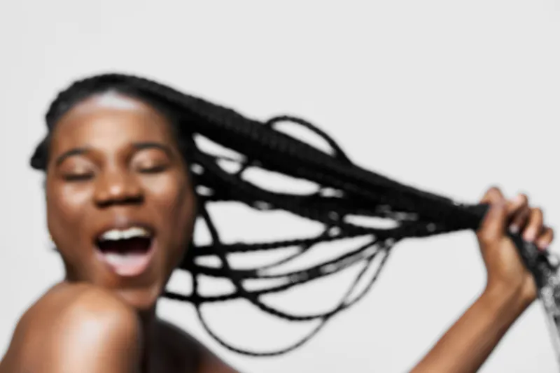 Joyful young African woman with braids expressing happiness and energy against a neutral background, celebrating beauty and self expression
