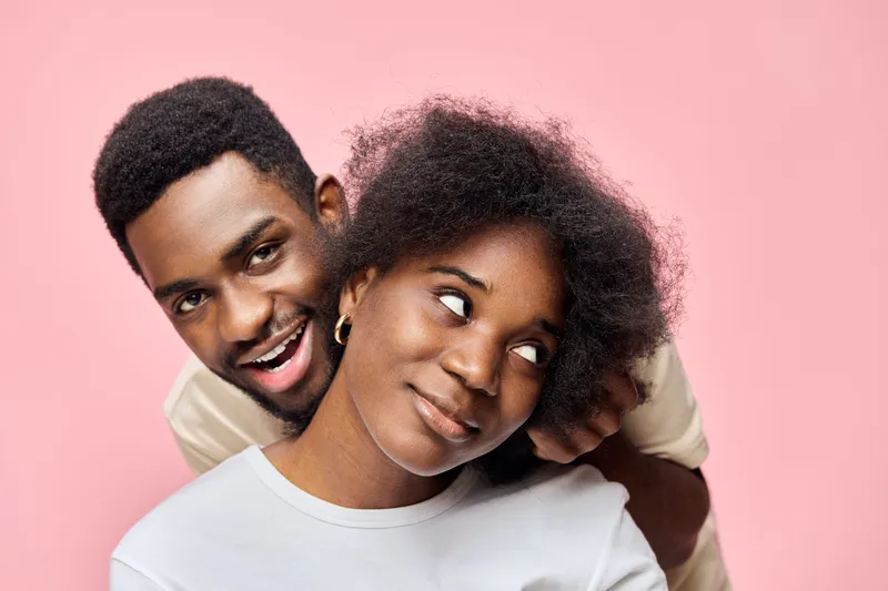 Happy couple with natural hairstyles against a pink background, showcasing Afro textured hair, love, and joy in a modern setting