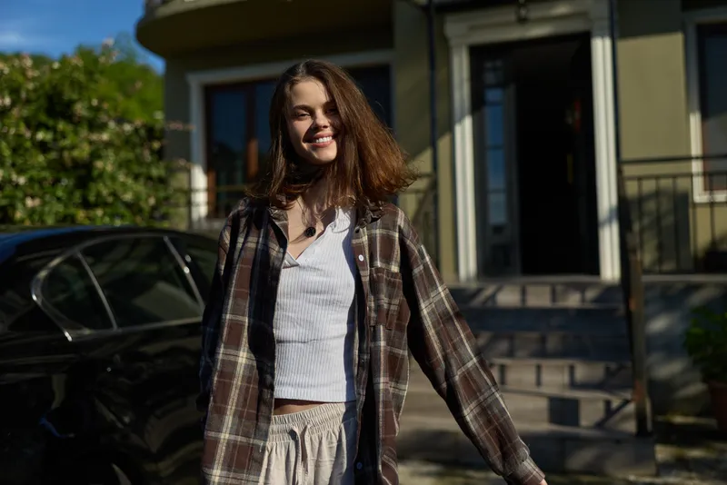 Smiling woman with wavy hair wearing a plaid jacket outdoors. Casual lifestyle scene on a sunny street, relaxed mood, and everyday fashion