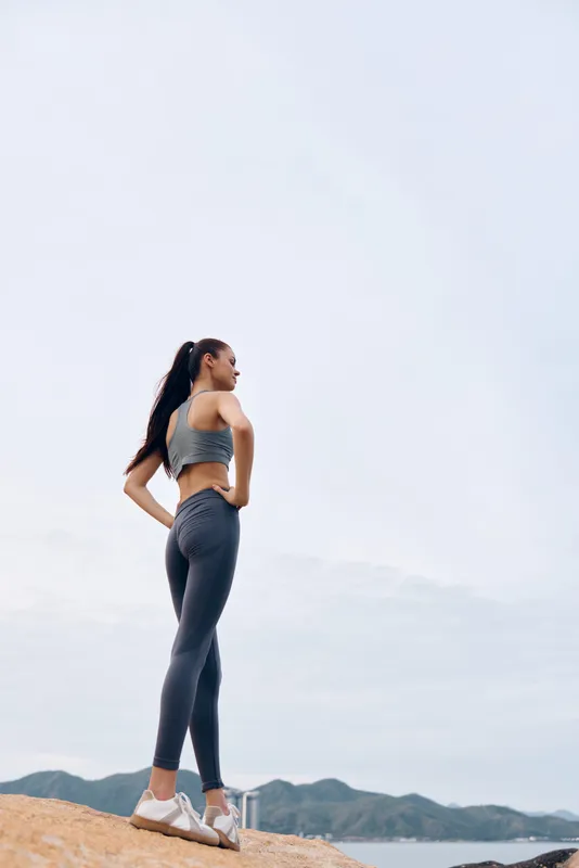 Fitness model in activewear poses confidently outdoors, showcasing strength and determination against a serene background, emphasizing exercise and health