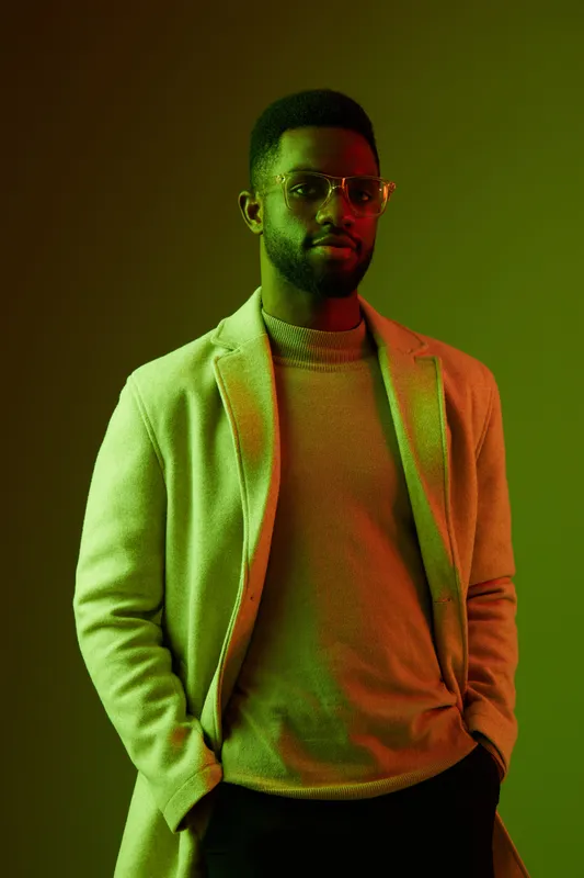 Stylish man in a green lit studio wearing modern attire and glasses, exuding confidence and sophistication in a fashion forward concept