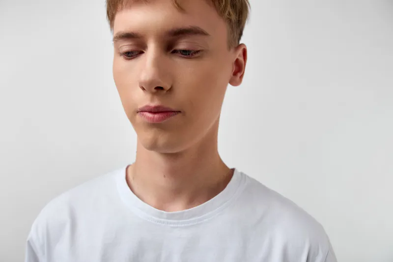 Young man wearing a white t shirt with a thoughtful expression in a studio setting, against a clean background, conveying calm, focus, and minimalism for lifestyle branding.