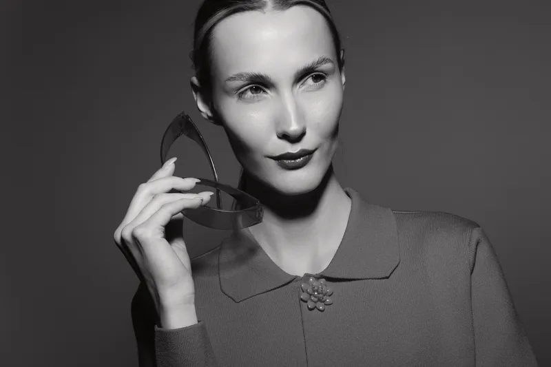 White woman with fair skin holding a transparent geometric shape near her face, posing in studio lighting for fashion and art concept.